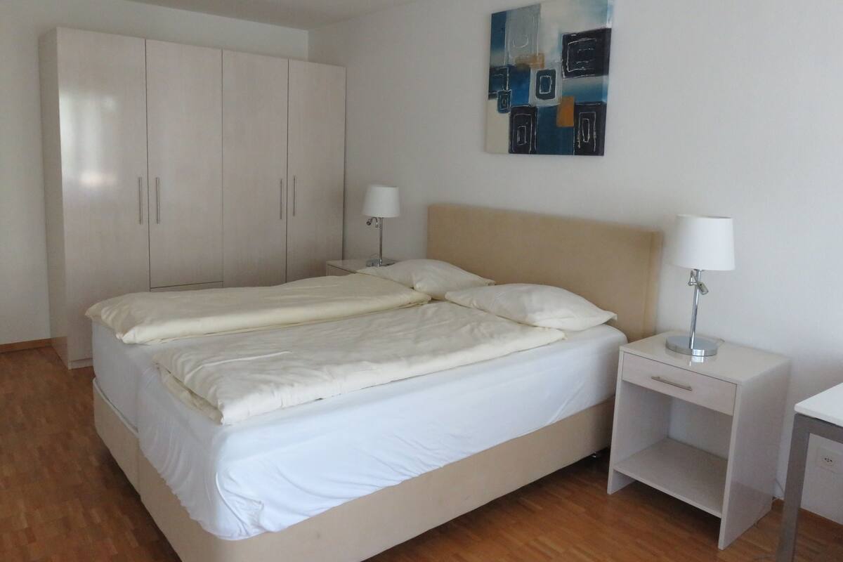 Ein Schlafzimmer mit einem Doppelbett, zwei Nachttischen mit Lampen, einem Kleiderschrank und einem Bild an der Wand.