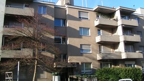 A multi-story residential building with balconies, a tree in front, and a clear sky. - Swiss Star District 11 (Zürich)