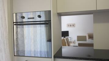 Une cuisine moderne dotée d’un four encastré, d’un plan de travail et donnant sur un espace chambre avec un lit et un téléviseur.