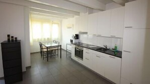 A kitchen with white cabinets, a dining table with chairs, and a black cabinet. - Swiss Star District 11 (Zürich)