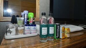 Una encimera de baño con artículos de aseo, incluyendo botellas de loción, una lata de refresco y un cepillo para el cabello.