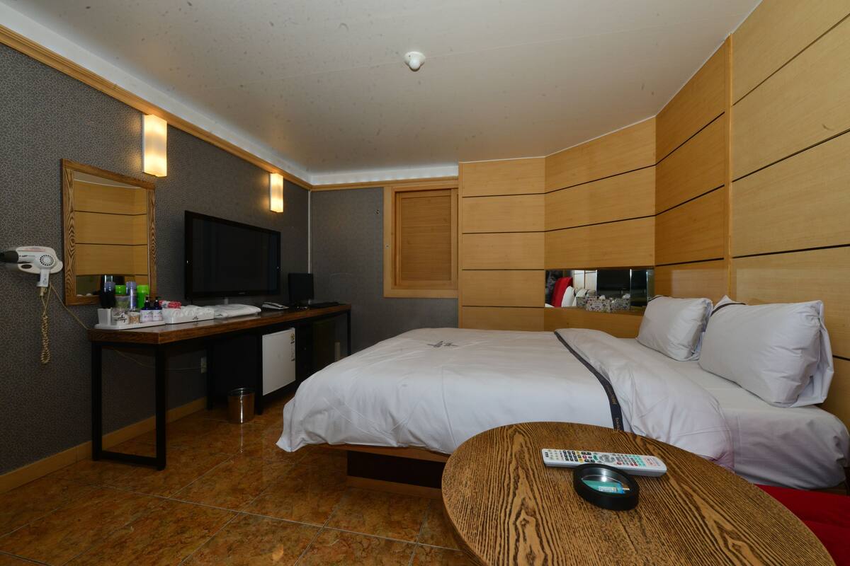 Ein Hotelzimmer mit Bett, Schreibtisch mit Fernseher, Spiegel und einem kleinen Tisch mit Fernbedienung.
