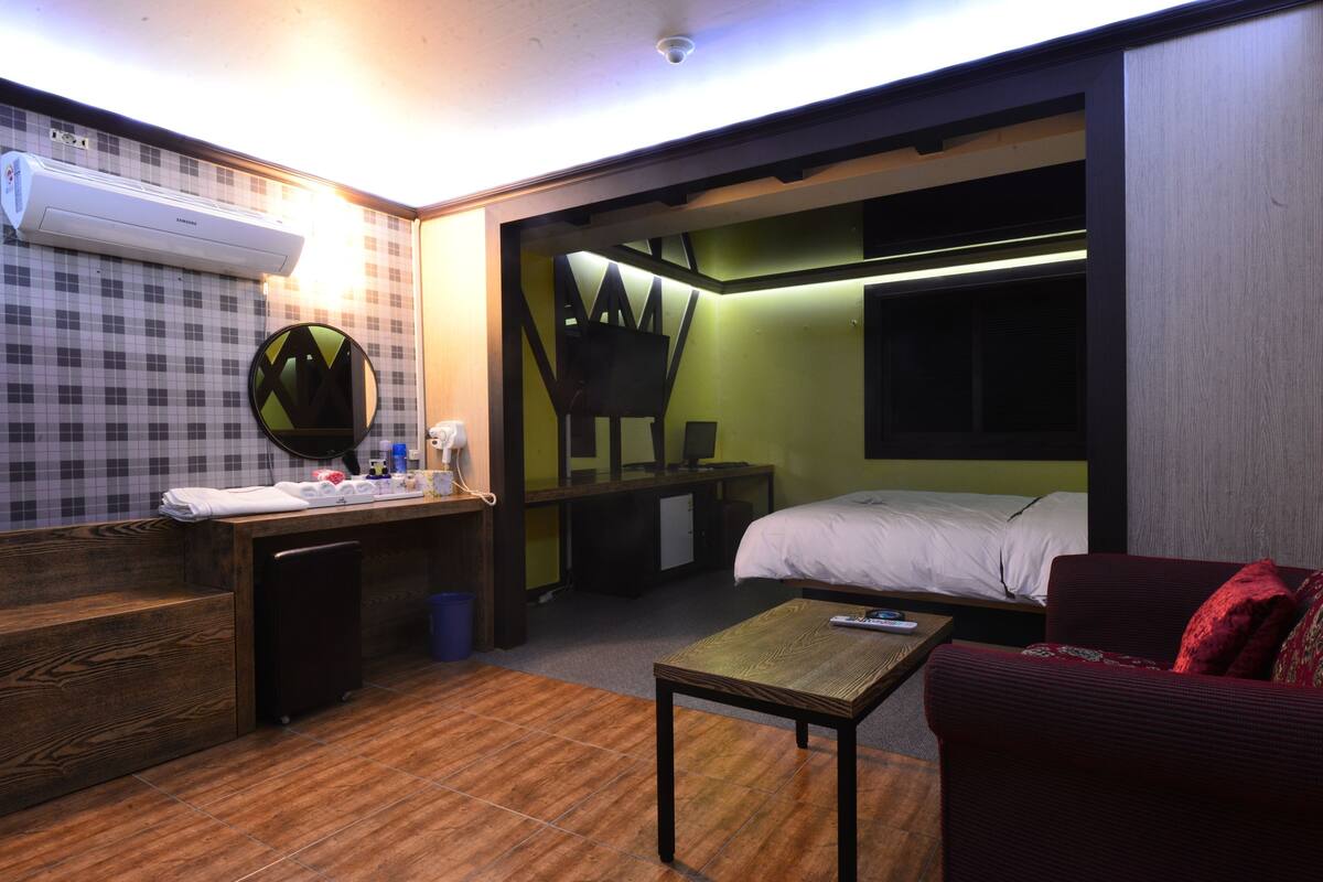 Ein kleines Hotelzimmer mit Bett, Schreibtisch mit Computer, einem kleinen Tisch und einer Couch.