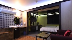 Habitación de hotel compacta con cama, pequeño escritorio, silla, sofá y espejo.