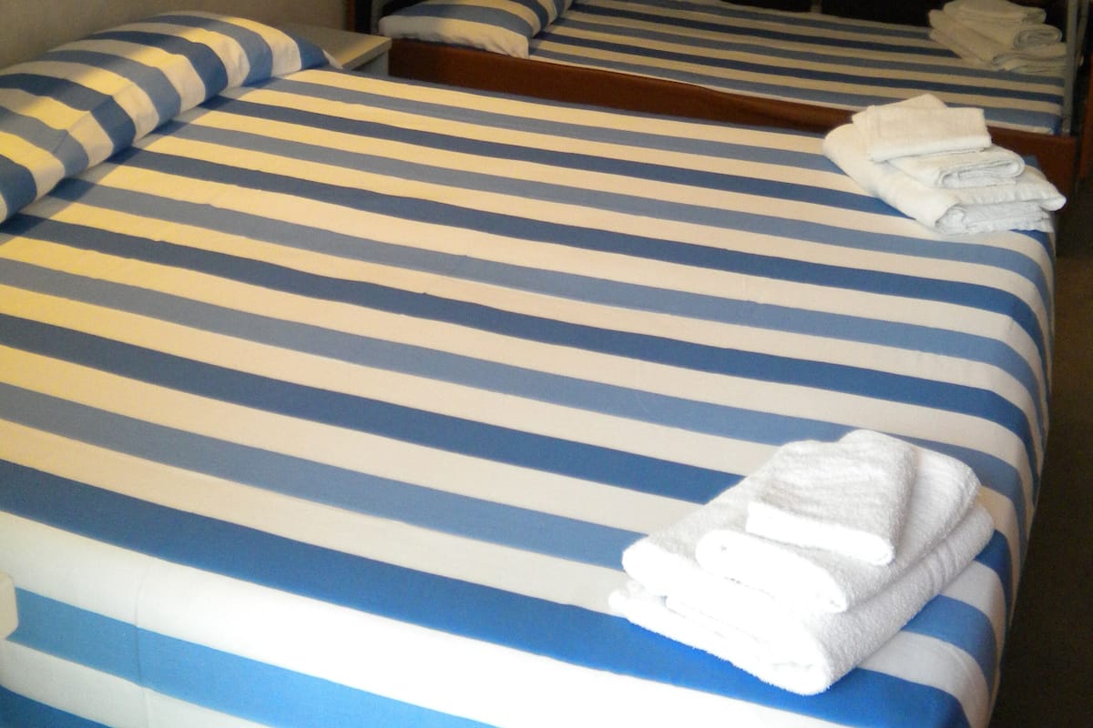 Habitación con literas, ropa de cama a rayas y toallas dobladas con cuidado en la litera inferior.