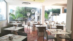 A restaurant with multiple tables and chairs, large windows, and decorative heart-shaped lights. - Hotel Ambasciata (Riccione)