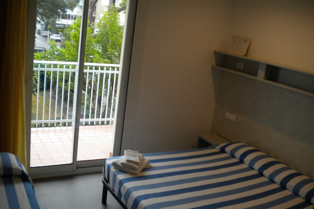 Habitación de hotel con cama, mesita de noche y vista al balcón exterior.