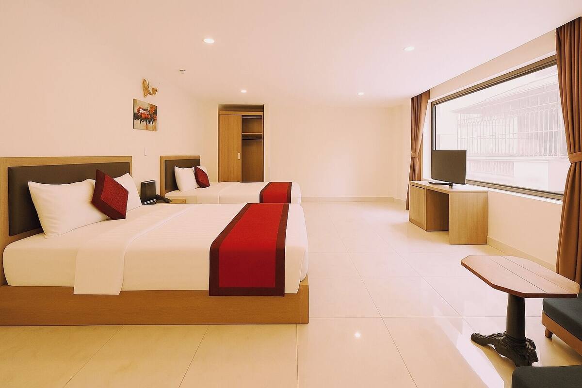 A hotel room with two beds, a desk, a TV, and a window with curtains.