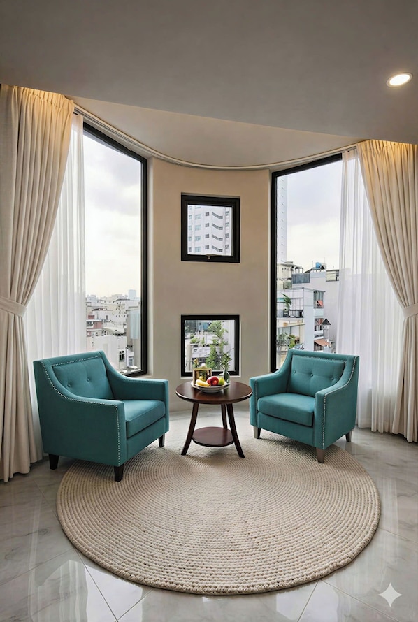 Una sala de estar moderna con dos sillones azul verdoso, una mesa redonda de centro y un ventanal con cortinas.