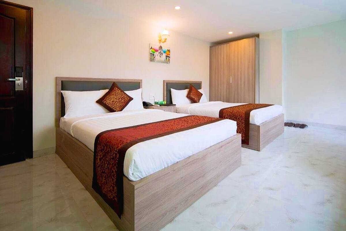 A hotel room with two beds, each with a wooden headboard and white bedding. There is a wooden wardrobe and a wall-mounted light fixture.
