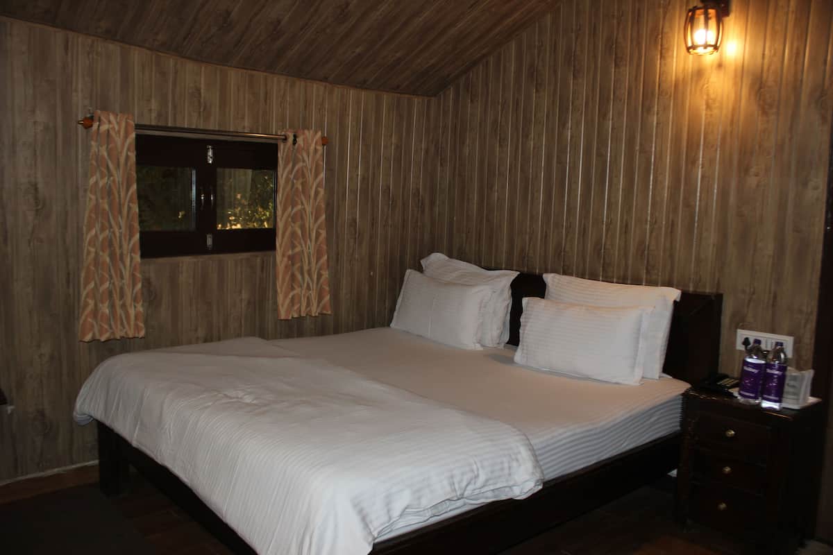 A bedroom with a wooden ceiling, a bed with white bedding, a nightstand with toiletries, and a window with curtains.
