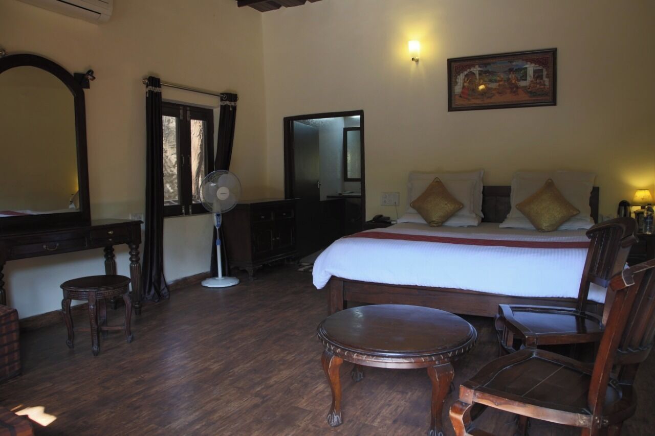 A hotel room with a large bed, wooden furniture, a desk, a chair, a small table, a mirror, and a painting on the wall.