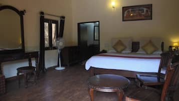 A hotel room with a large bed, wooden furniture, a desk, a chair, a small table, a mirror, and a painting on the wall.