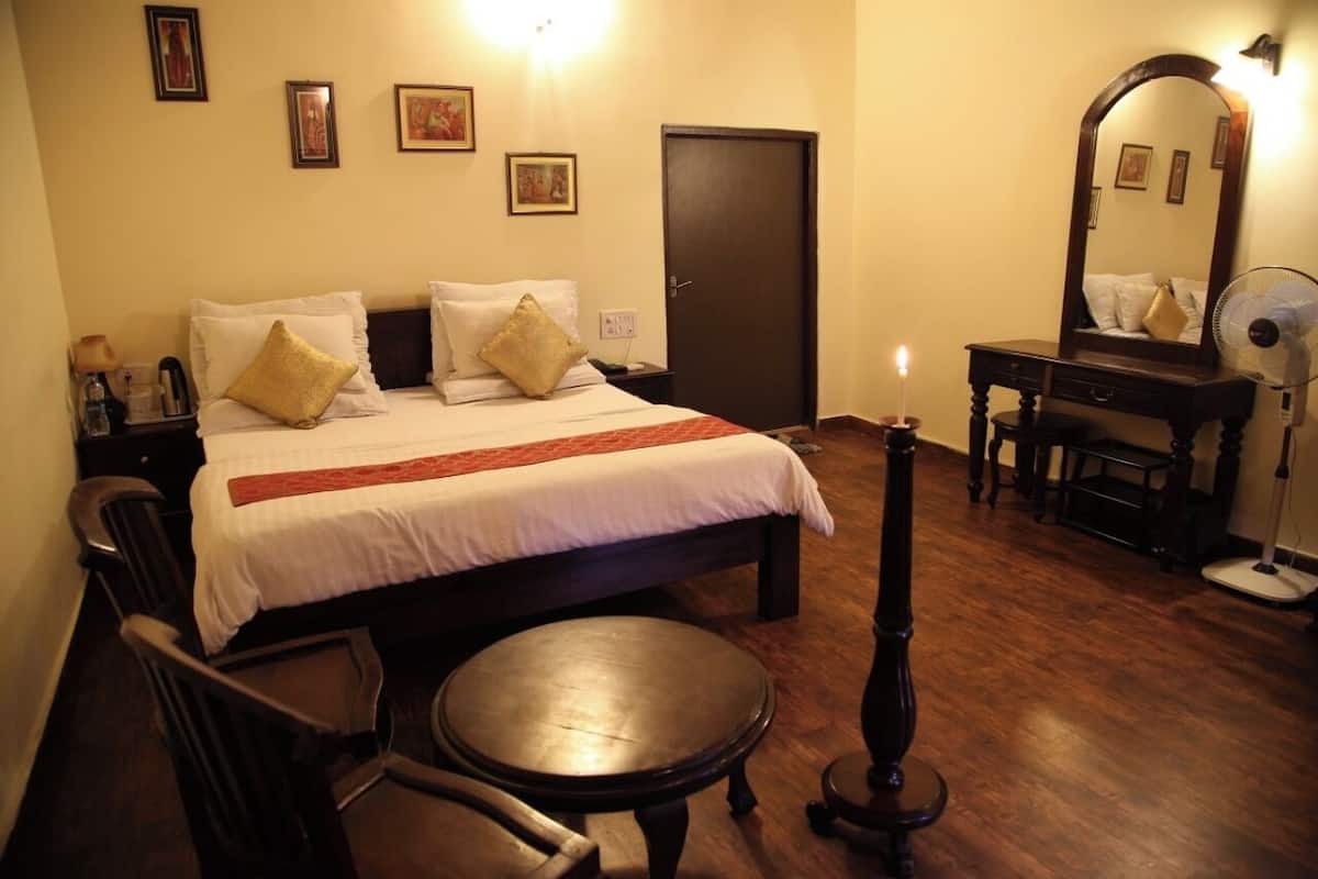 A hotel room with a large bed, a wooden chair, a small round table, a dresser, and a mirror.