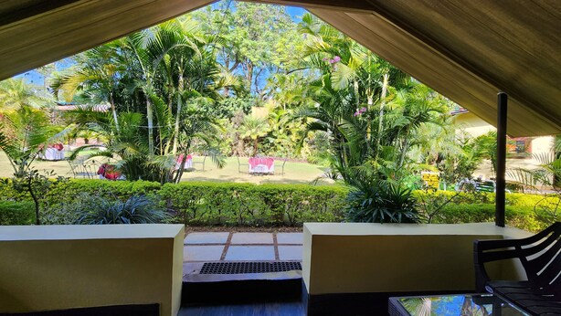 An outdoor seating area with a view of a garden and a building in the background. - Hill 'N' You - A Boutique Garden Resort (Abu Road)