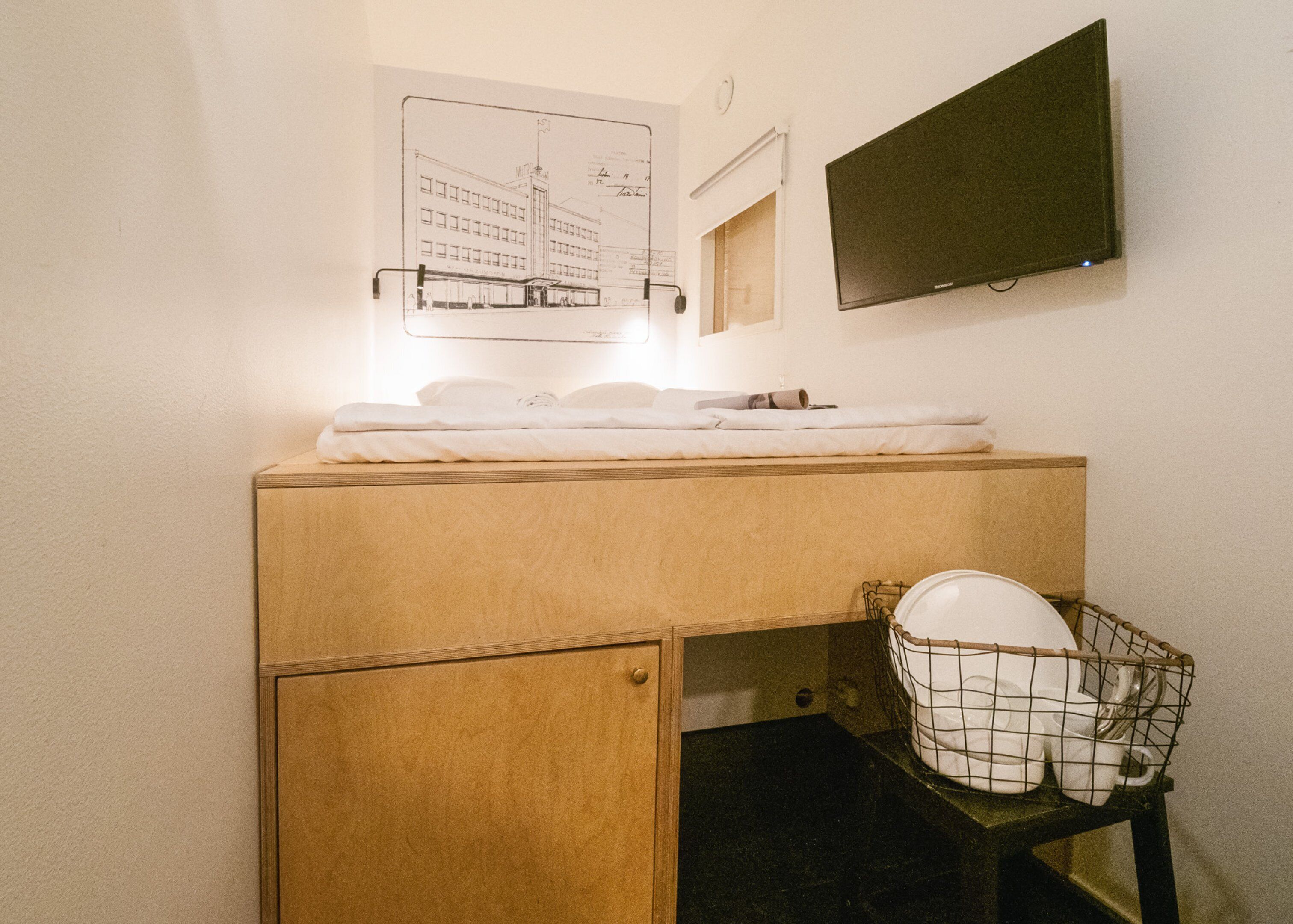 A small bathroom with a wooden cabinet, a sink, and a mirror. There is a framed architectural drawing on the wall above the sink.