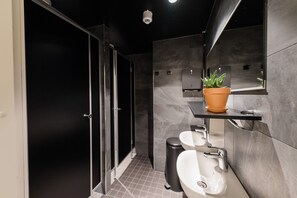 A modern bathroom with a glass shower enclosure, a white sink, and a potted aloe vera plant on a shelf. - Forenom Hostel Jyväskylä (Jyväskylä)