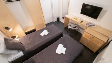 A compact hotel room with two single beds, a desk with a chair, a TV, and a small wooden cabinet.