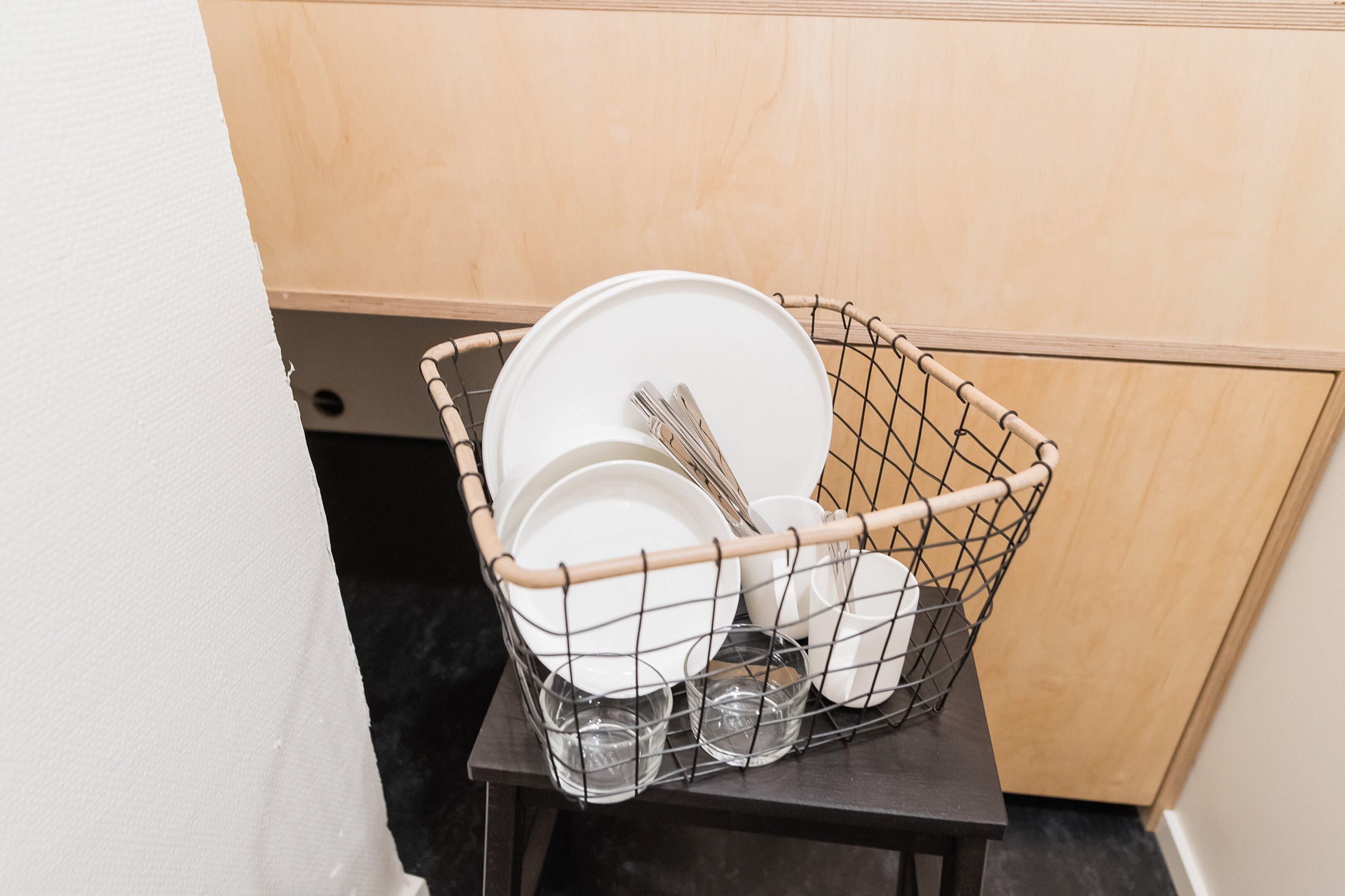 A wire basket containing plates, bowls, and glasses on a small table.