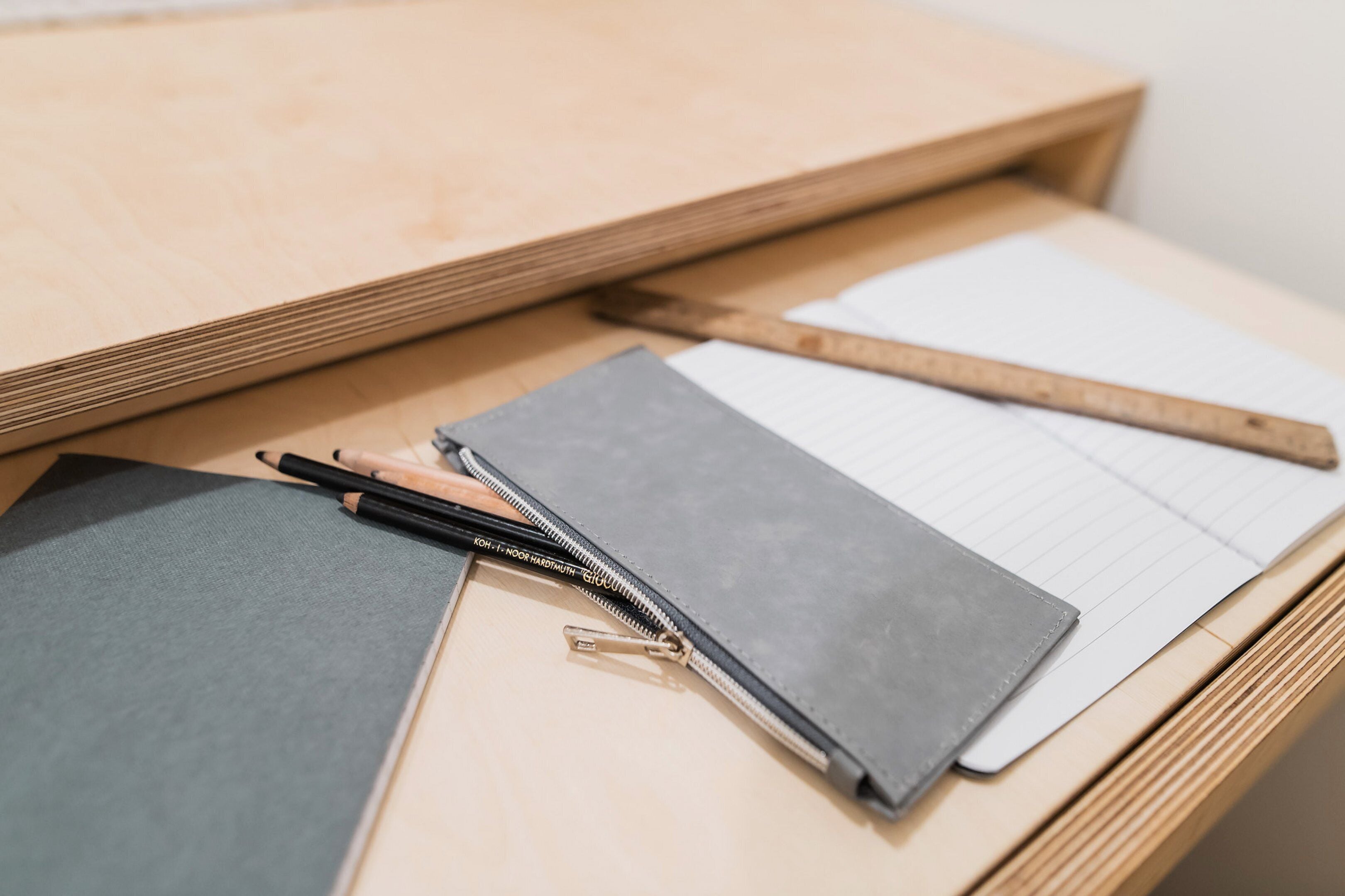 A wooden desk with a notebook, pencils, and a ruler.