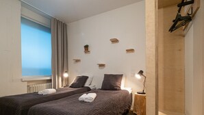A hotel room with two beds, a window with curtains, a radiator, and a small bedside table with a lamp. - Forenom Hostel Jyväskylä (Jyväskylä)