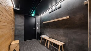 A modern bathroom with dark tiled walls, wooden benches, and a black door. - Forenom Hostel Jyväskylä (Jyväskylä)