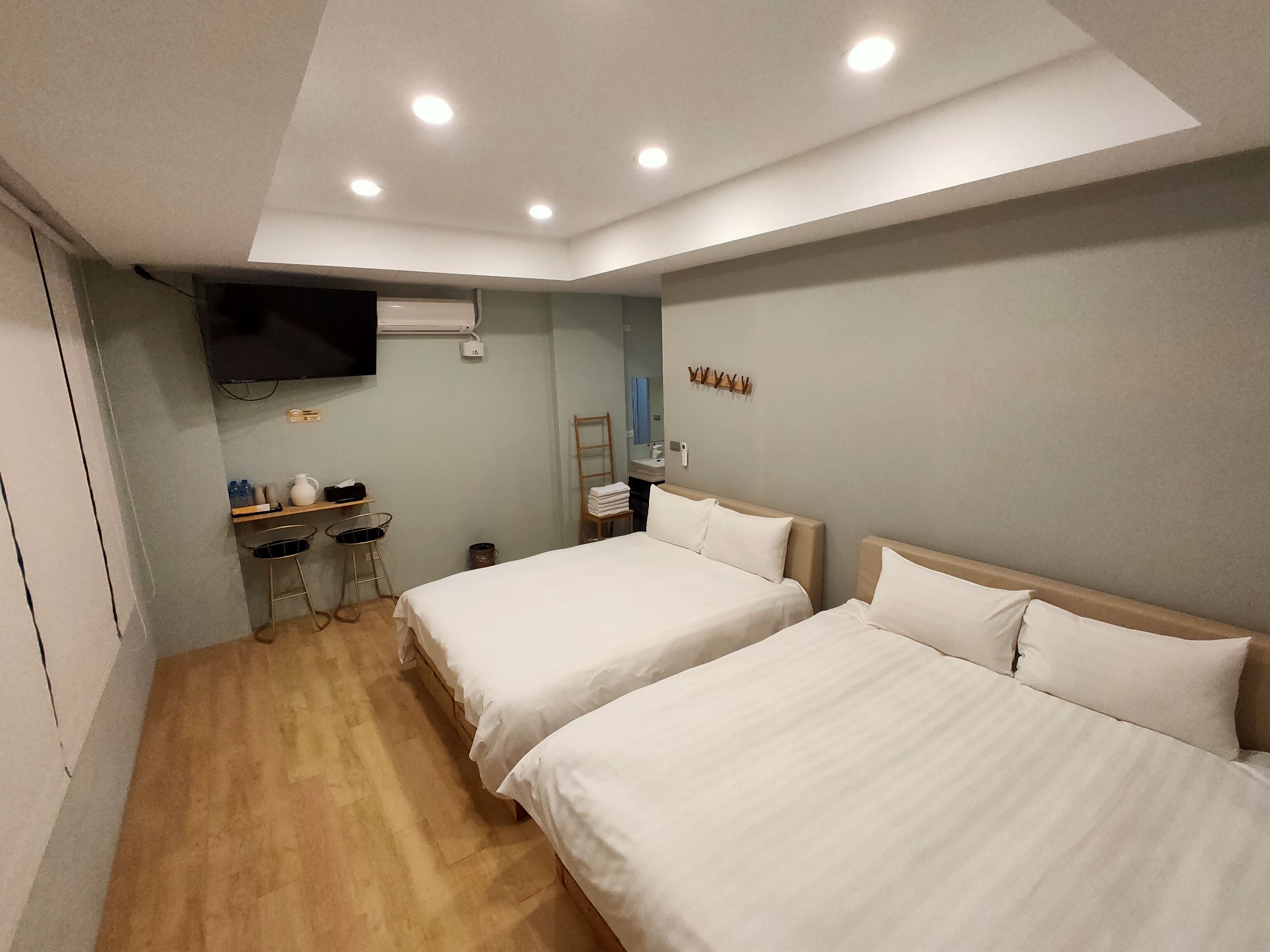 A hotel room with two beds, a desk with a chair, a TV, and a small bathroom area.