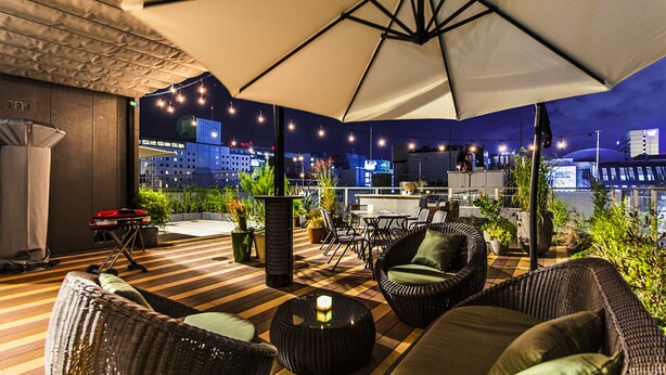 An outdoor patio with wicker furniture, a table, and a large umbrella. - H Hotel (Fukuoka)