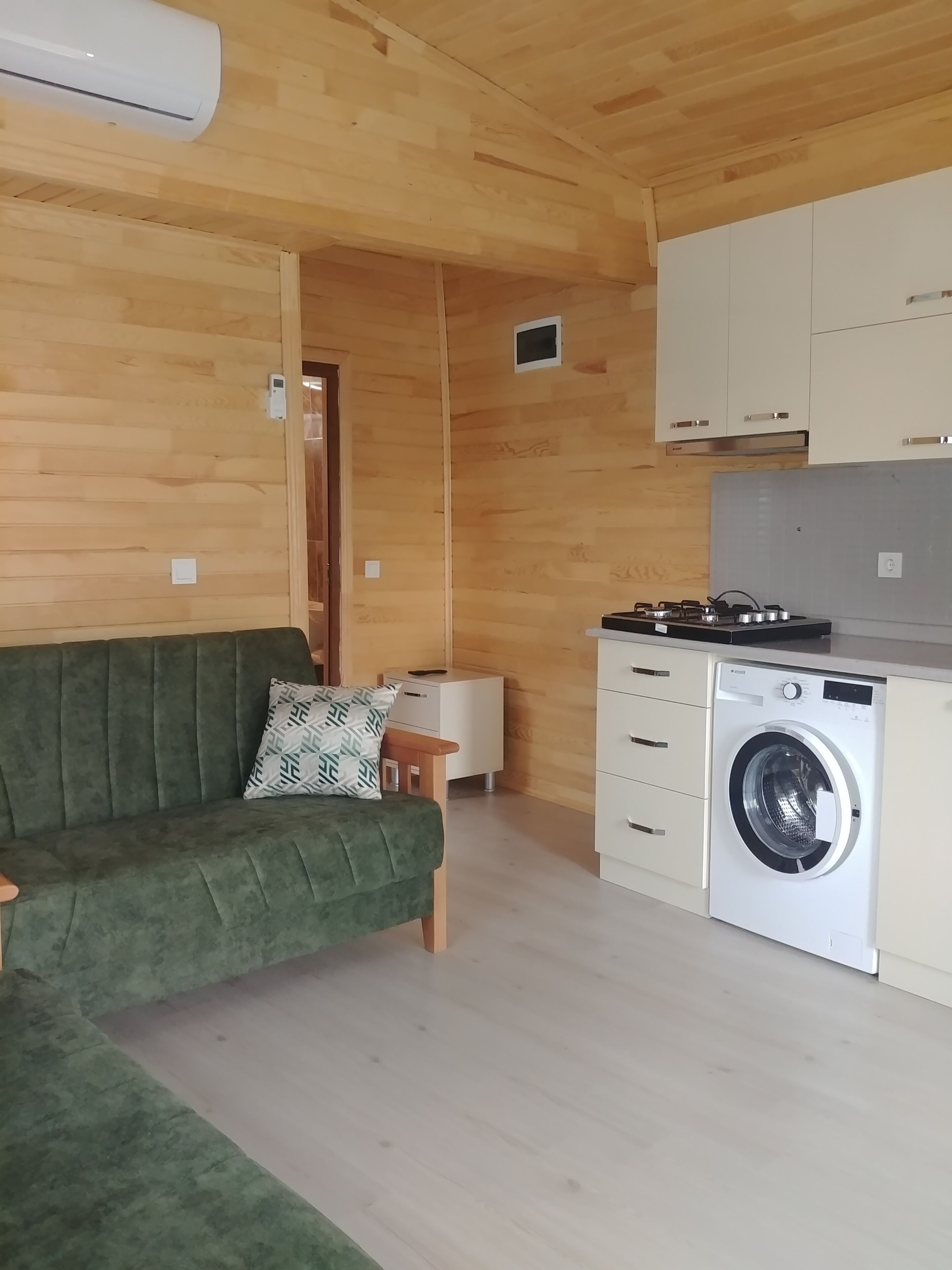 Ett kompakt bostadsutrymme med en grön soffa, en tvättmaskin och träväggar.
