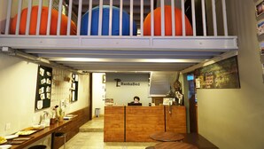 A hotel lobby with a reception desk, a wooden counter, a seating area, and a balcony with large decorative spheres.