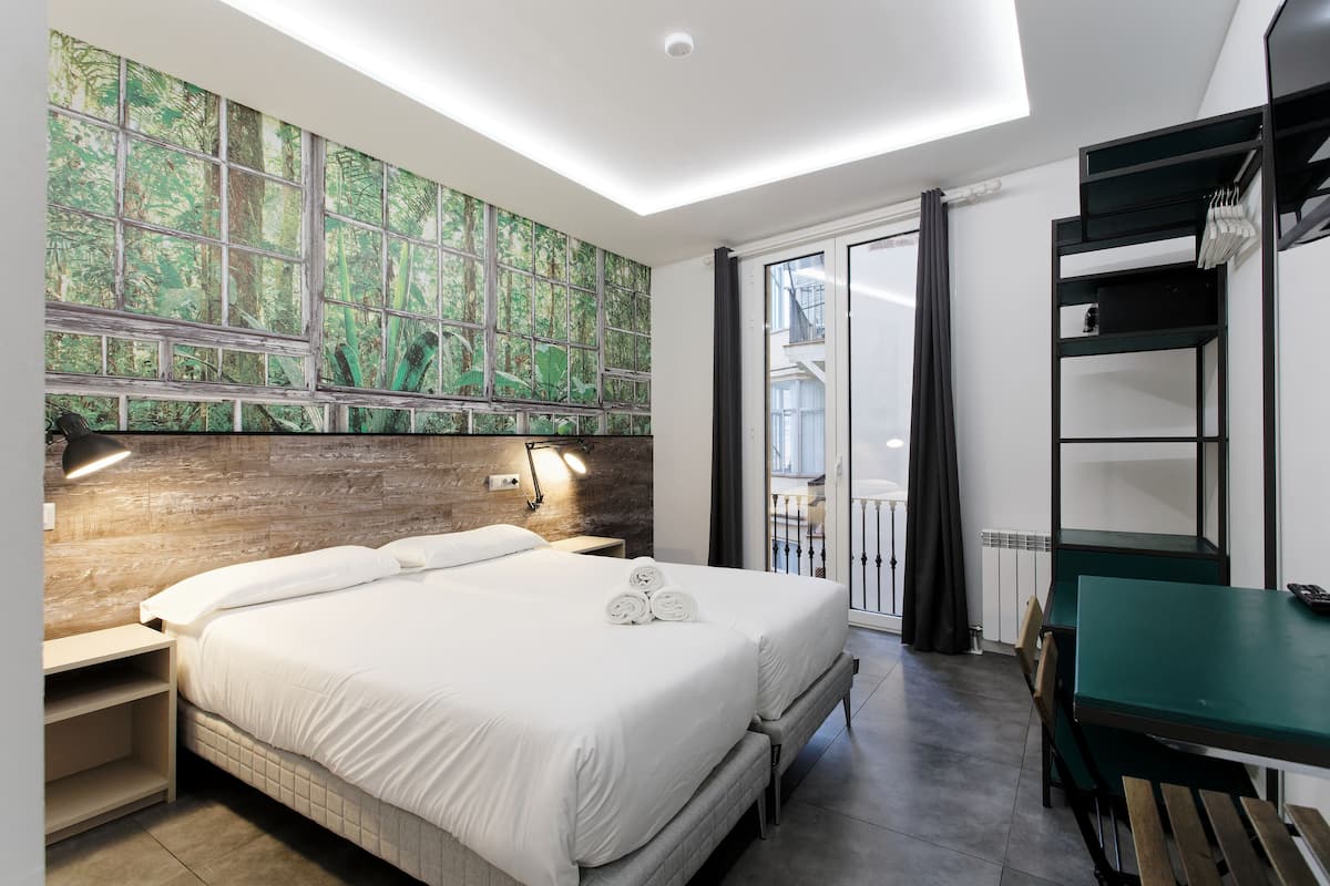 A modern hotel room with a large bed, a desk, and a balcony with a view.