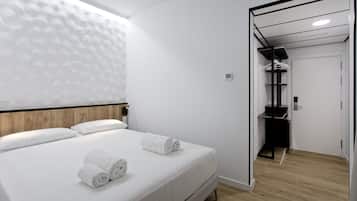 Una habitación de hotel moderna con una cama bien hecha, un cabecero de madera y una pared blanca con textura.