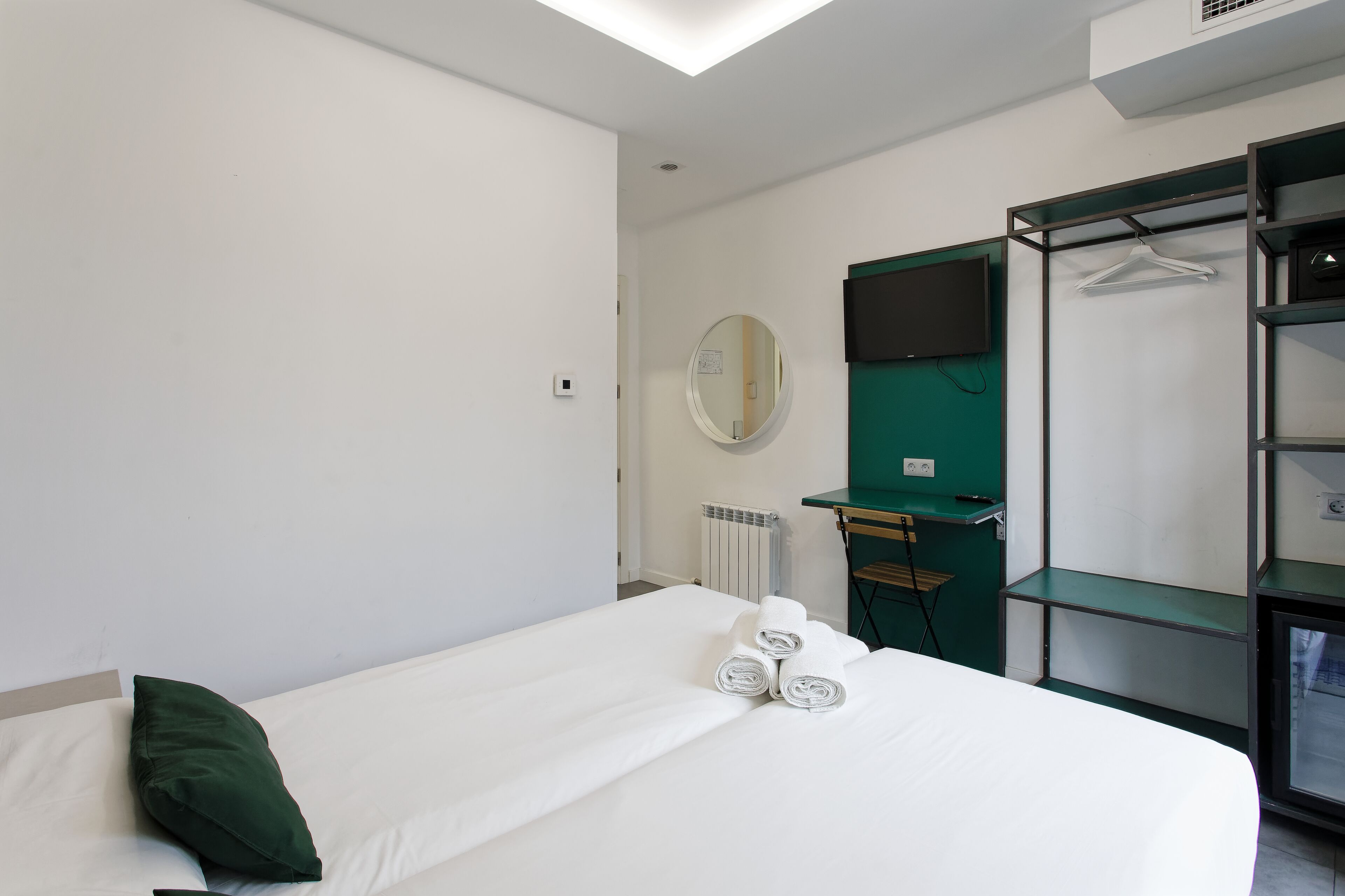 Una habitación de hotel con una cama, almohada verde, un espejo, televisor y armario.