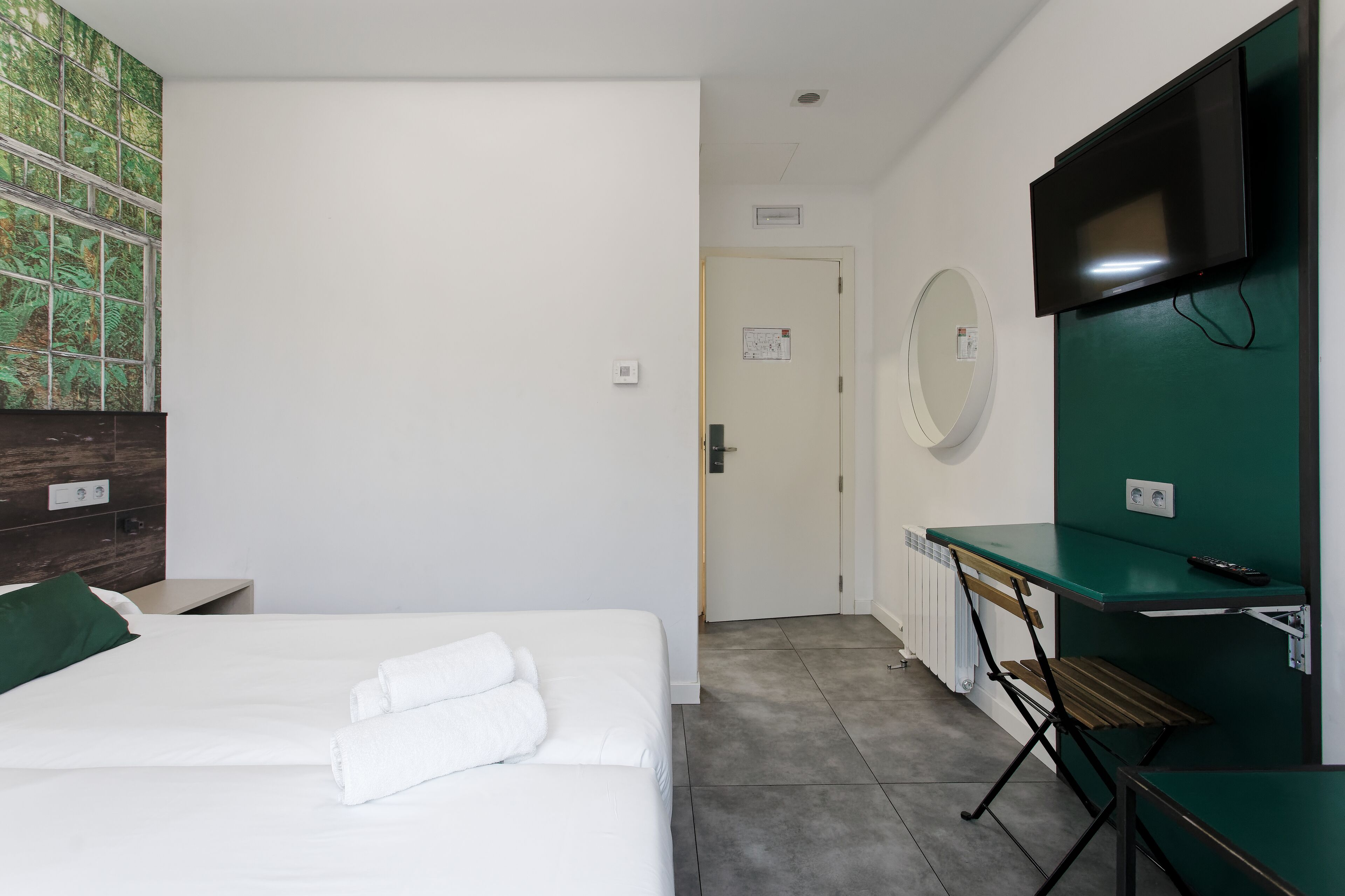 Een hotelkamer met een bed, een bureau, een televisie en een groene wand.