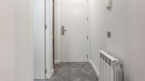 A narrow hallway with a white door at the end, a radiator on the right, and a light switch on the wall. - Fontanella Green House (Barcelona)