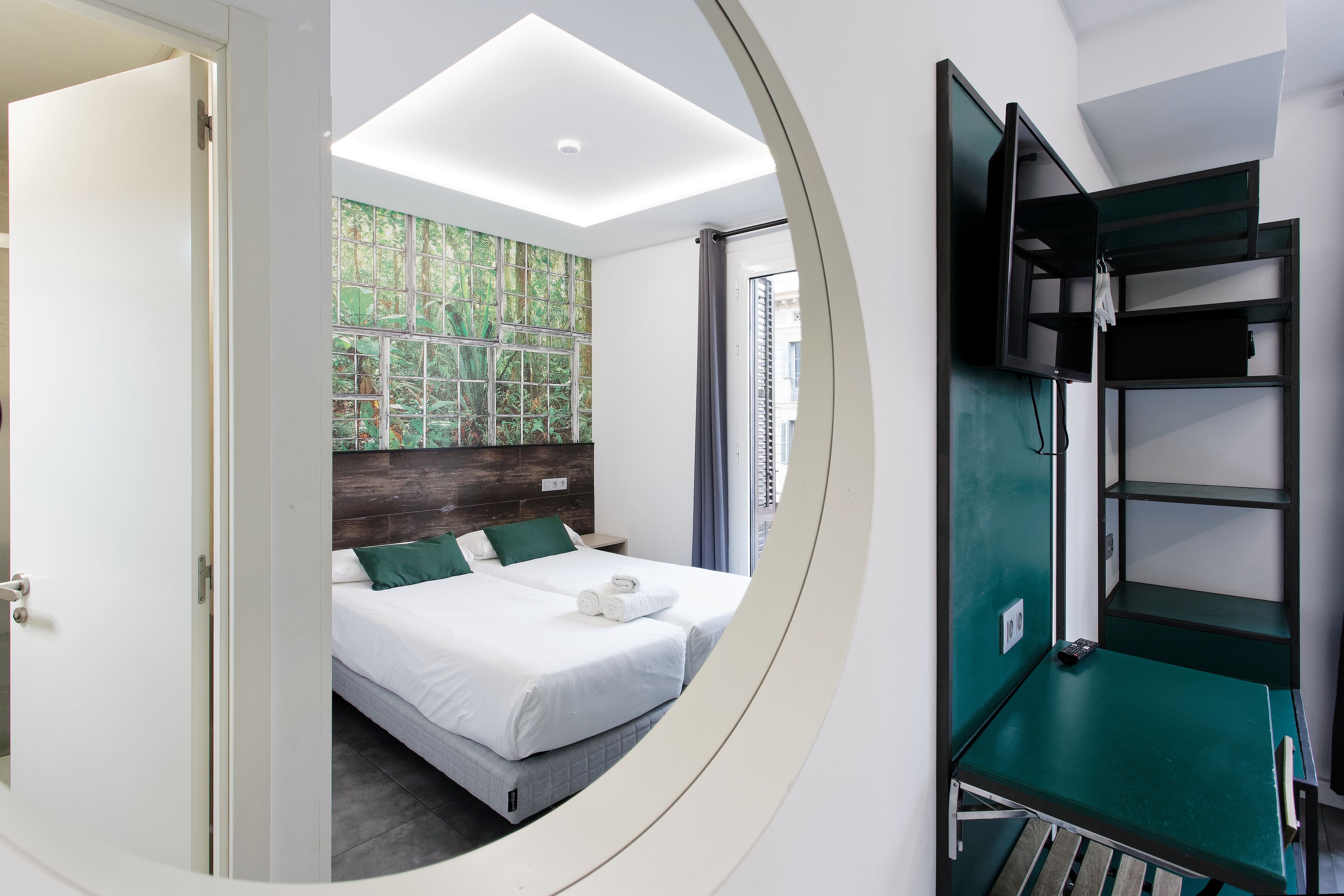 A modern hotel room with a bed, a green wall, a TV, and a mirror.