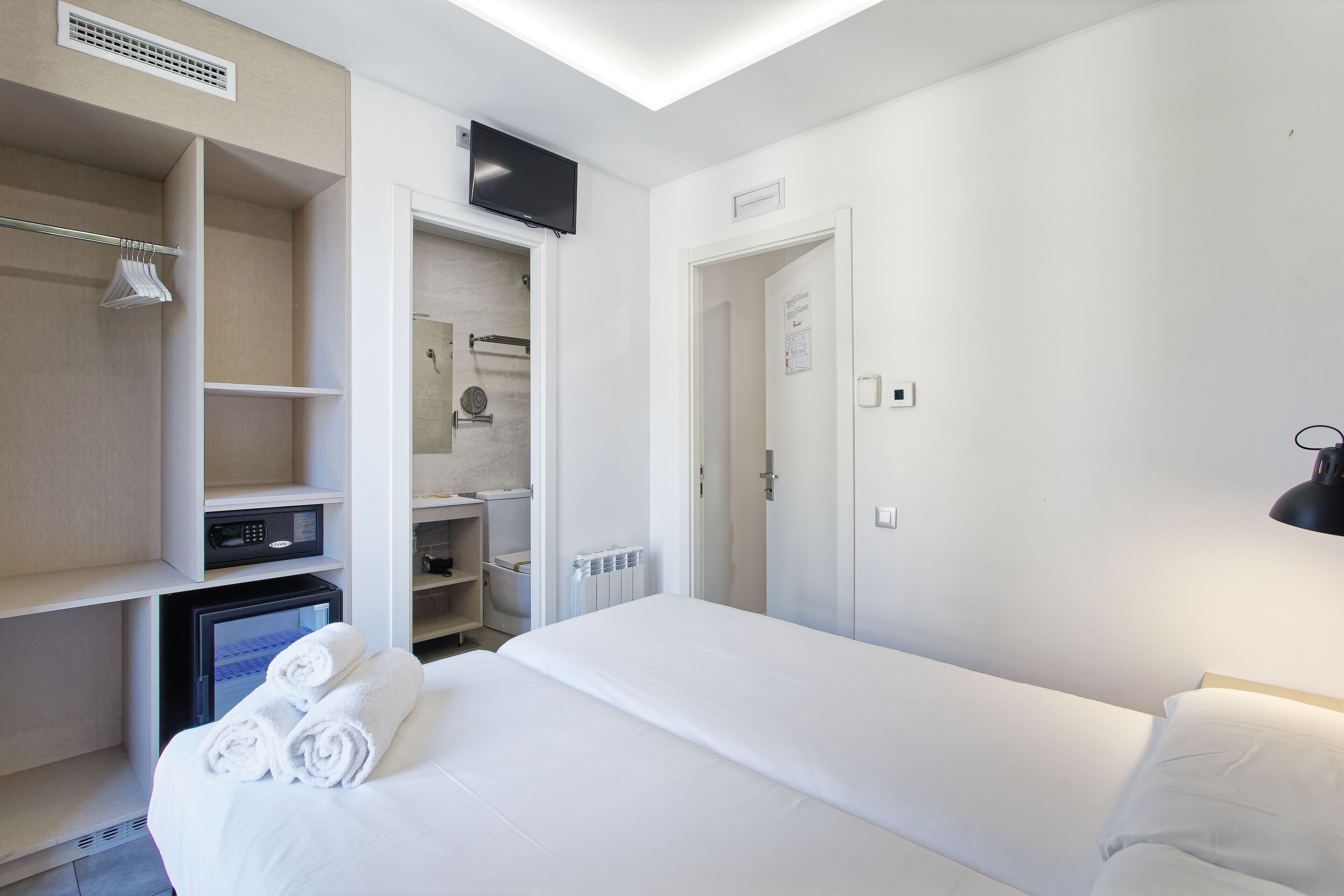 A hotel room with a bed, a TV mounted on the wall, a wardrobe, and a shower area.