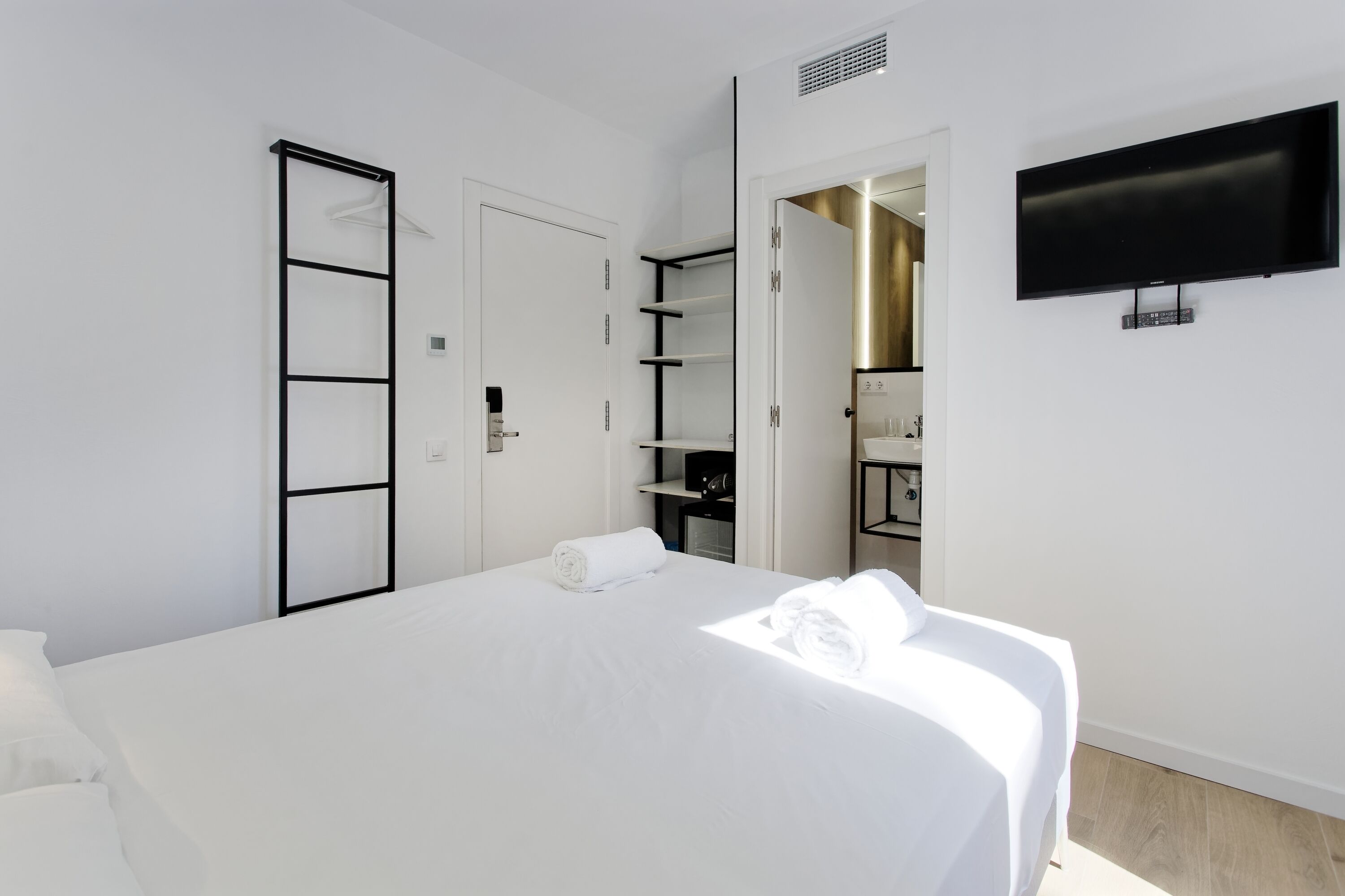 Una habitación de hotel moderna con una cama grande, un televisor montado en la pared y un vestidor con estantes.
