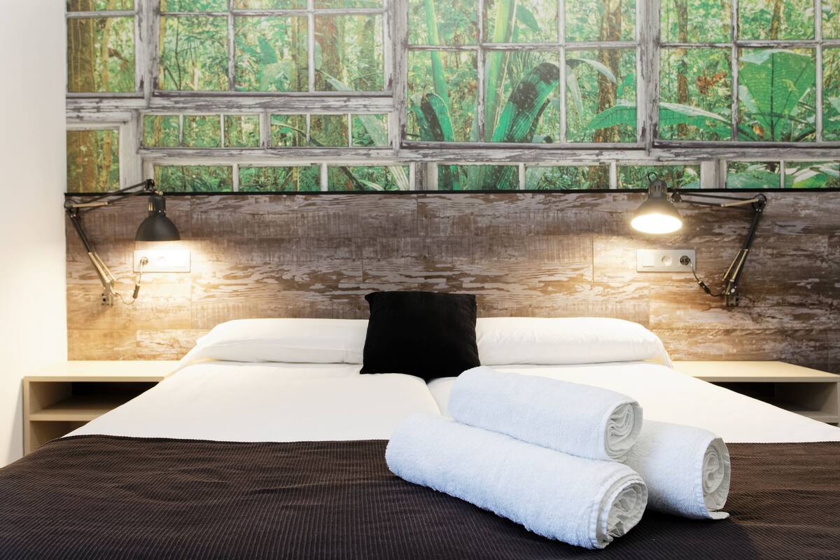 A hotel room with a large bed, two bedside lamps, a black pillow, and rolled towels.
