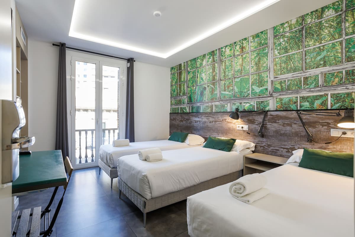 A hotel room with two beds, a dining table, and a view of the city through a large window.