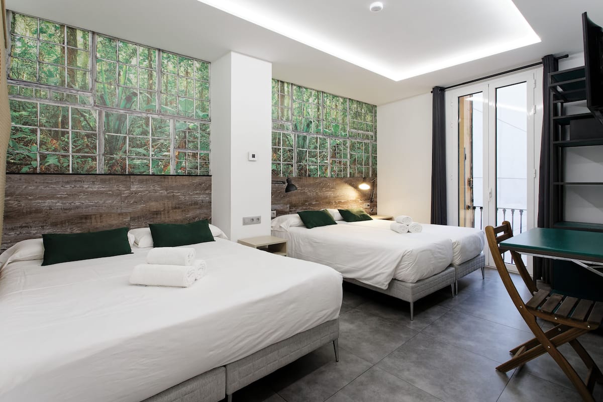 A modern hotel room with two beds, a dining table, and a large window with a forest view.