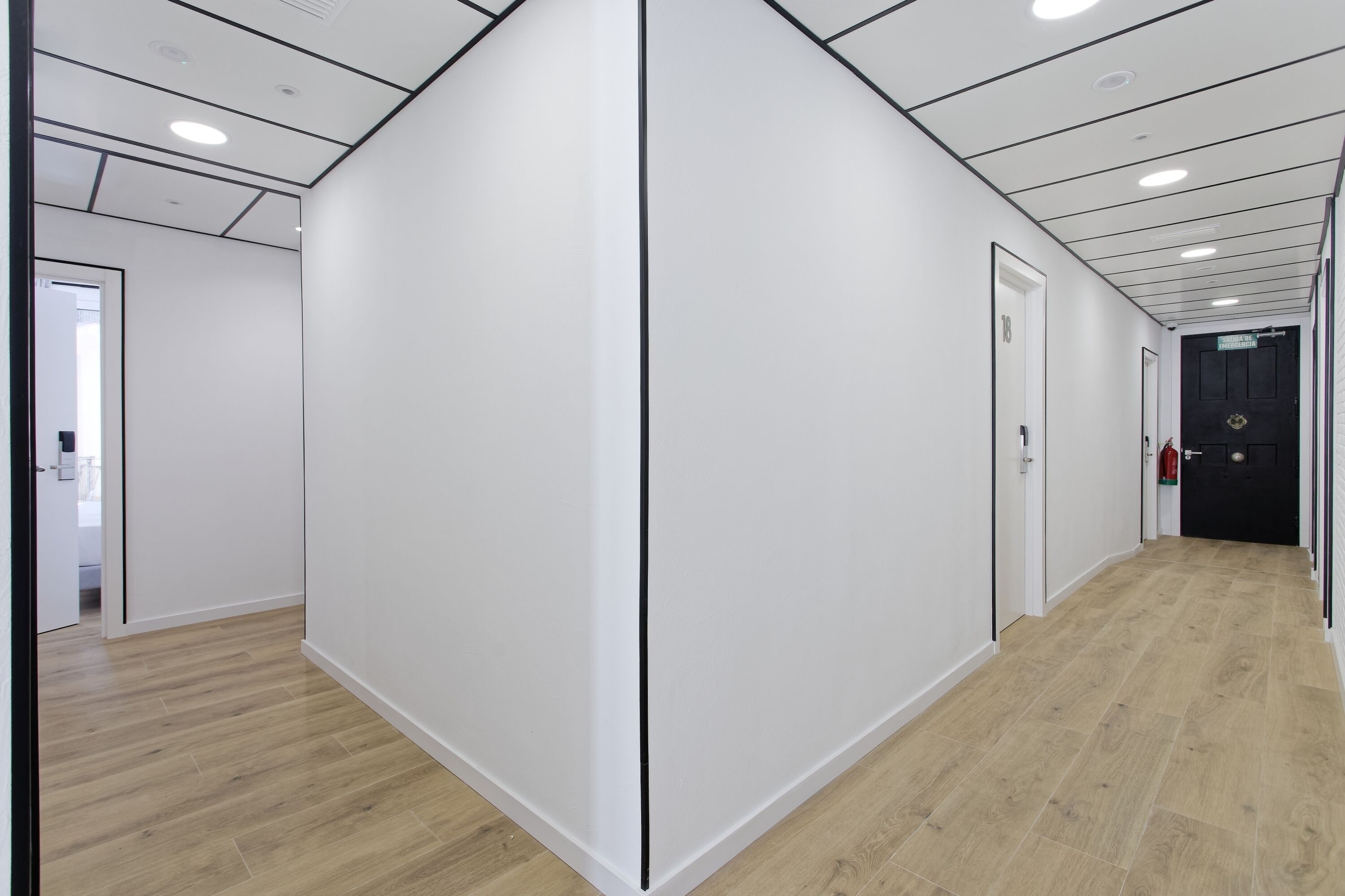 A modern hallway with white walls, wooden flooring, and recessed lighting.