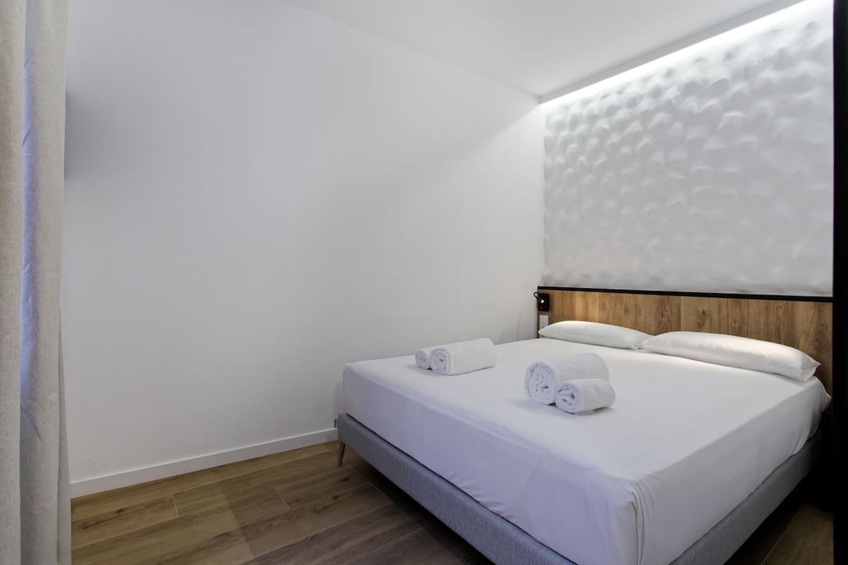 A hotel room with a neatly made bed, a wooden headboard, and a wooden floor.