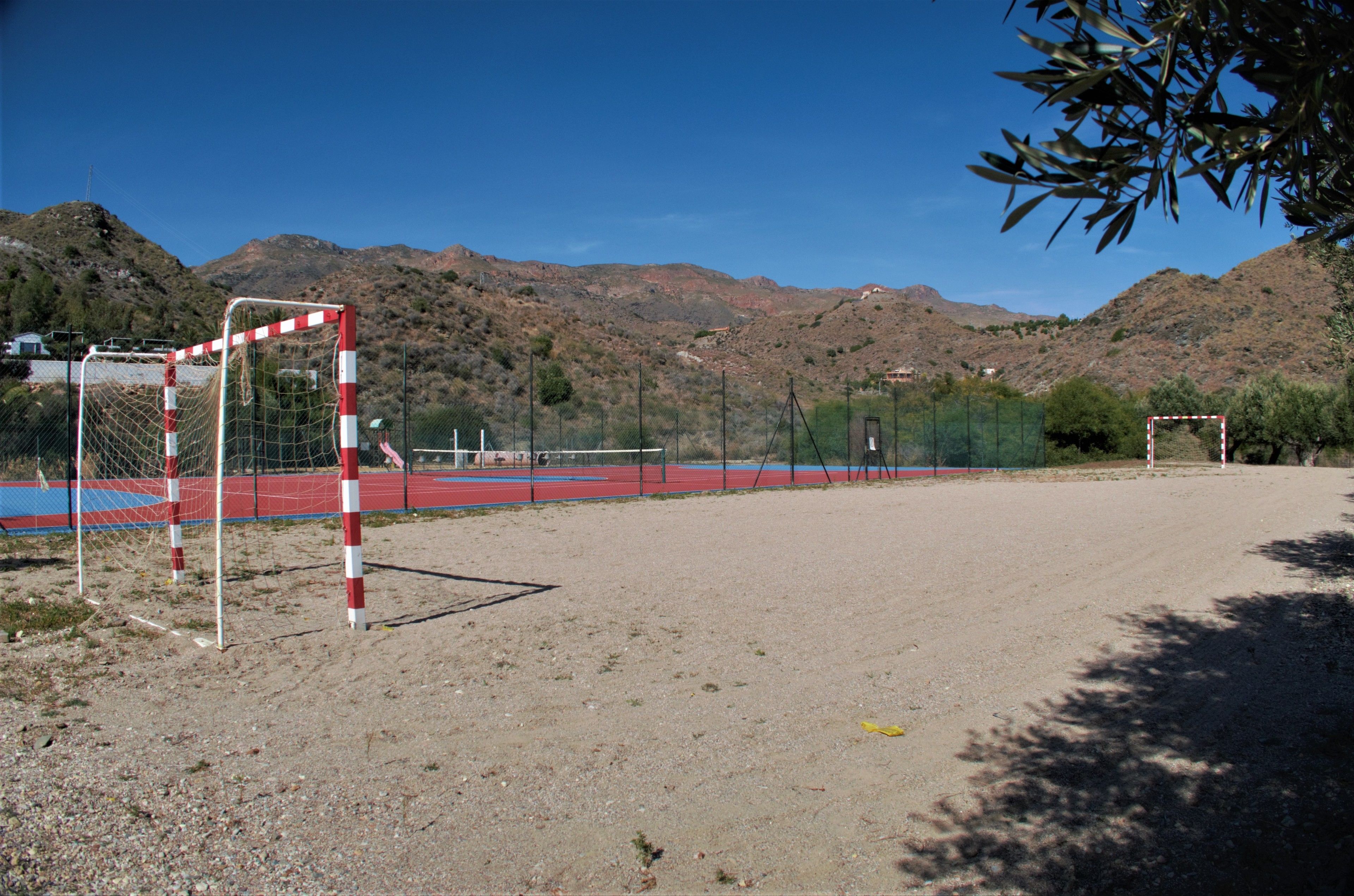 An outdoor sports field with a goalpost, surrounded by a fence, and a mountainous backdrop.