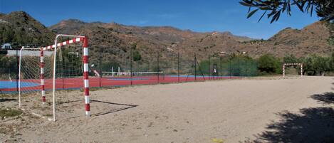 An outdoor sports field with a goalpost, surrounded by a fence, and a mountainous backdrop.