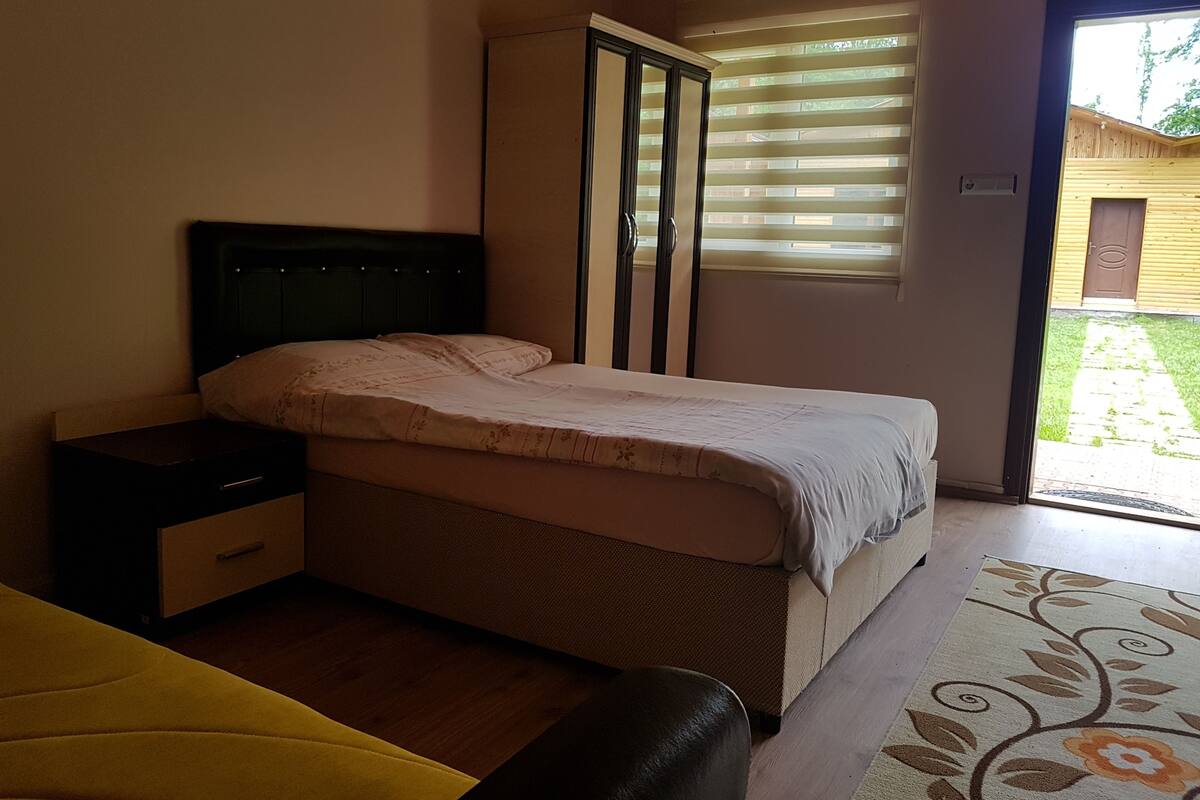 A bedroom with a bed, a nightstand, a wardrobe, and a window with blinds.