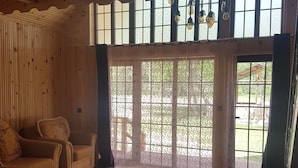 A wooden interior with a sofa, a patterned rug, and a large window with a view of the outdoors.