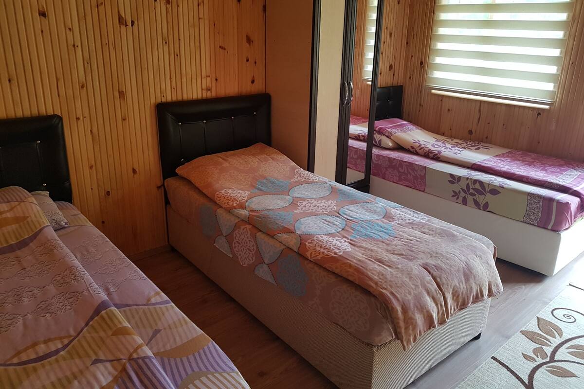 A room with two beds, wooden walls, a wardrobe, and a window with blinds.