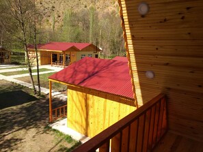 Una cabaña de madera con techo rojo, una terraza de madera y una vista de un edificio con techo similar al fondo.