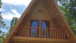 A wooden cabin with a balcony, large windows, and a stone foundation.